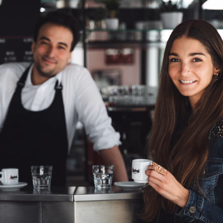 Imagebild Frau mit Kaffeetasse an einem Tresen, dahinter ein Mann