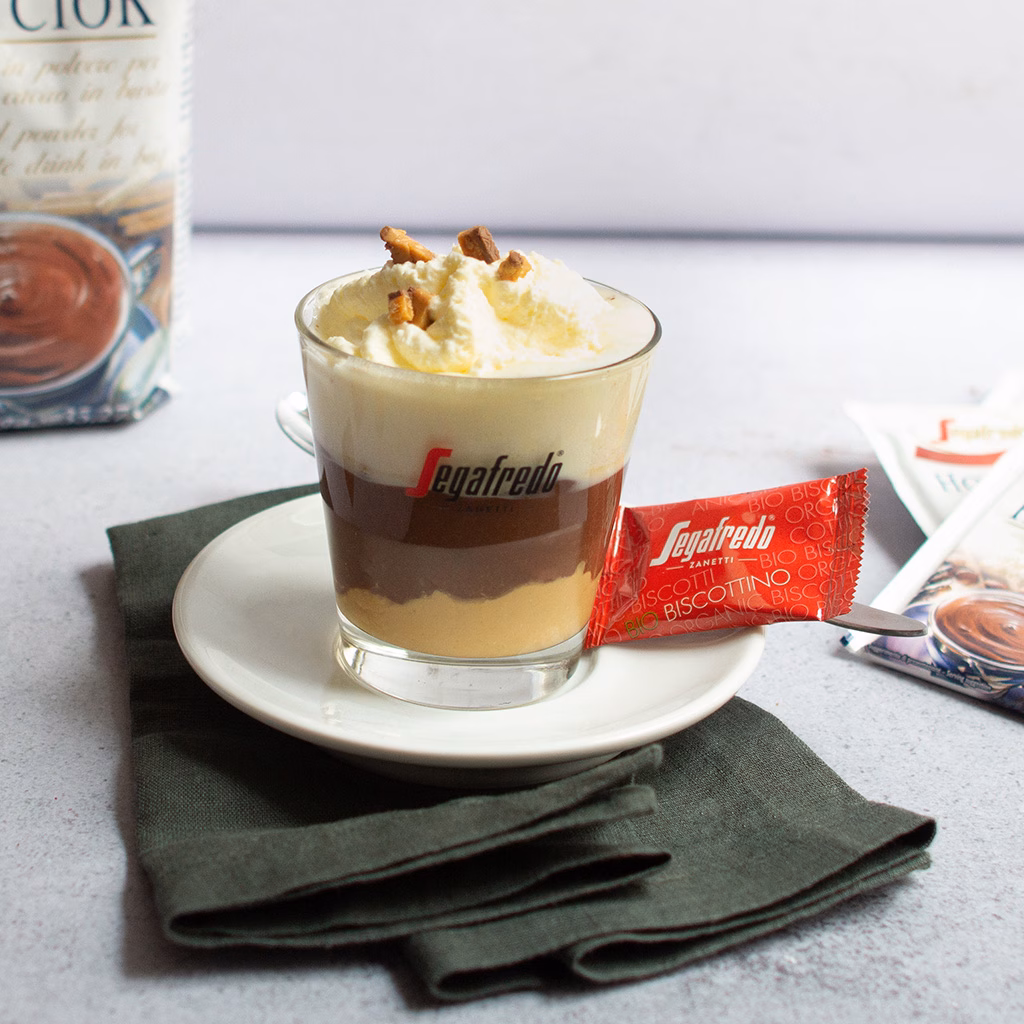 Imagebild Glas mit Erdnussbutter, heißer Schokolade und Schlagobers garniert mit Crumble, im Hintergrund Produktpackung