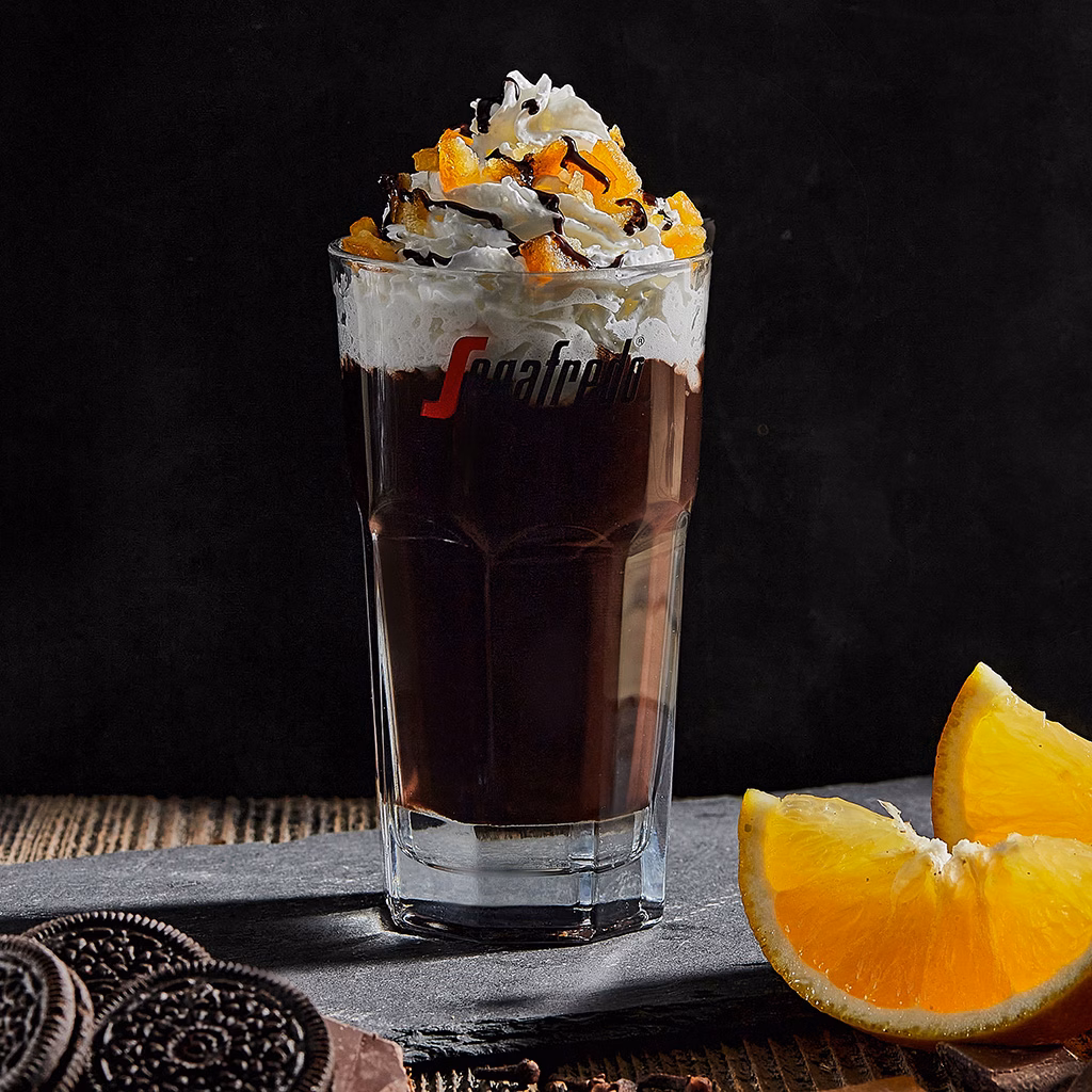Imagebild Glas mit Schokoladenpudding, Schlagobers und Orangenzesten auf einer Schieferplatte, Orangenstücke und Kekse im Vordergrund, dunkler Hintergrund