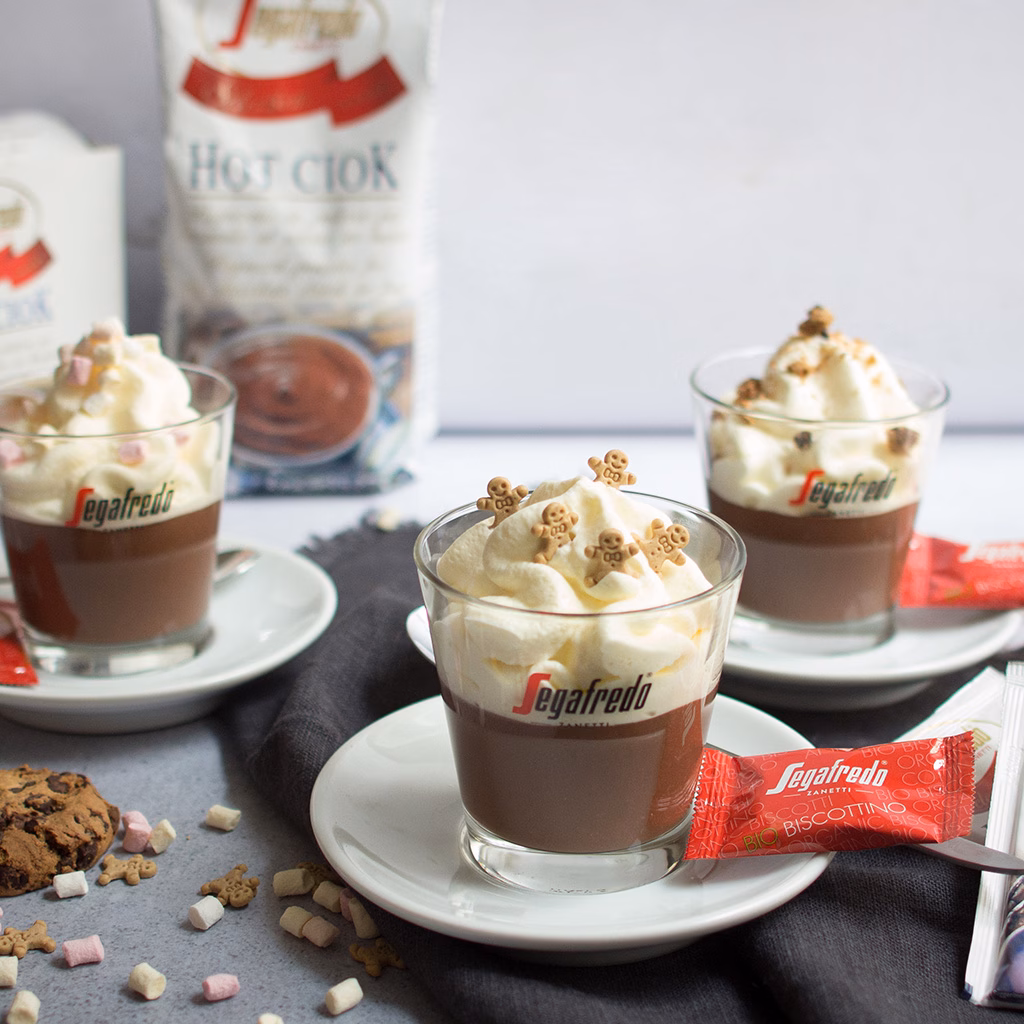 Imagebild Glas mit Schokoladenpudding und Schlagobers und Dekoration, im Hintergrund weitere Gläser und Produktpackung